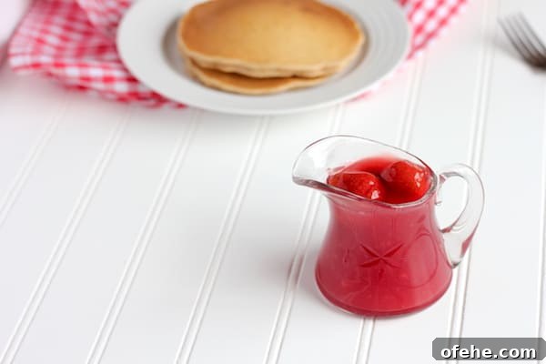 Homemade Strawberry Syrup Recipe for Pancakes & Drinks 2 Image shows a small glass vessel with strawberry sauce next to a plate of pancakes