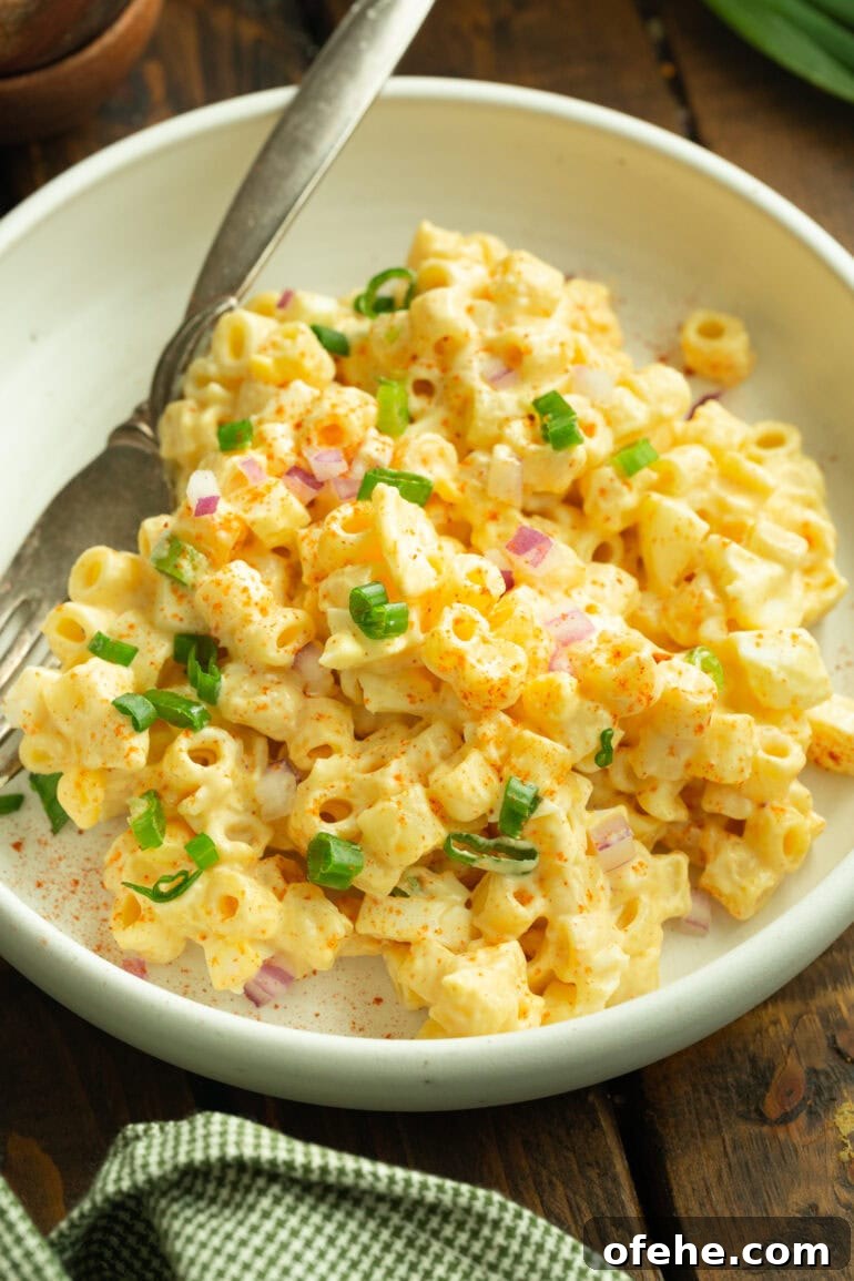 Deviled Egg Pasta Salad for Summer Gatherings 5 a photo of a serving of deviled egg pasta salad with a fork next to it in a shallow white bowl