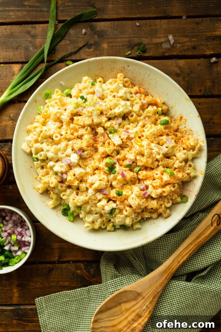 Deviled Egg Pasta Salad for Summer Gatherings 6 a photo of a large white bowl of creamy deviled egg pasta salad surrounded by a wooden spoon, green onions and the pasta salad garnishes
