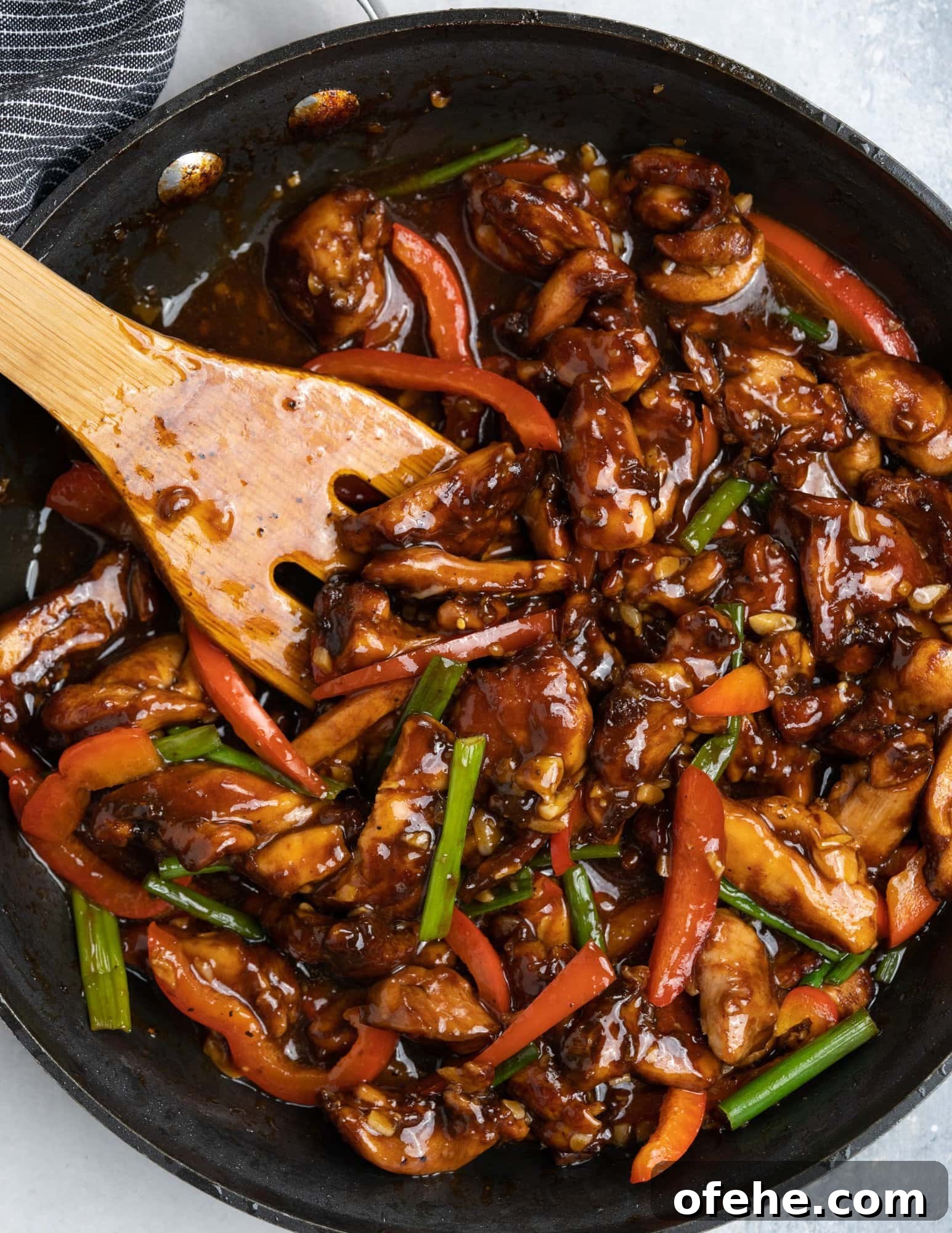 Chicken cooked in Chinese sauce with flavors from garlic in a black skillet and tossed with a wooden spatula