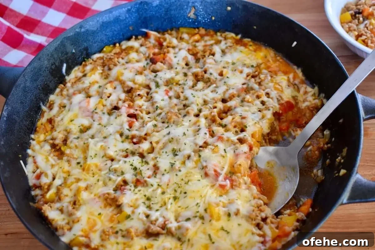 One-Pan Stuffed Pepper Skillet with Ground Beef and Rice 2 Stuffed Peppers Skillet recipe with melted cheese on top and a spoon in it.