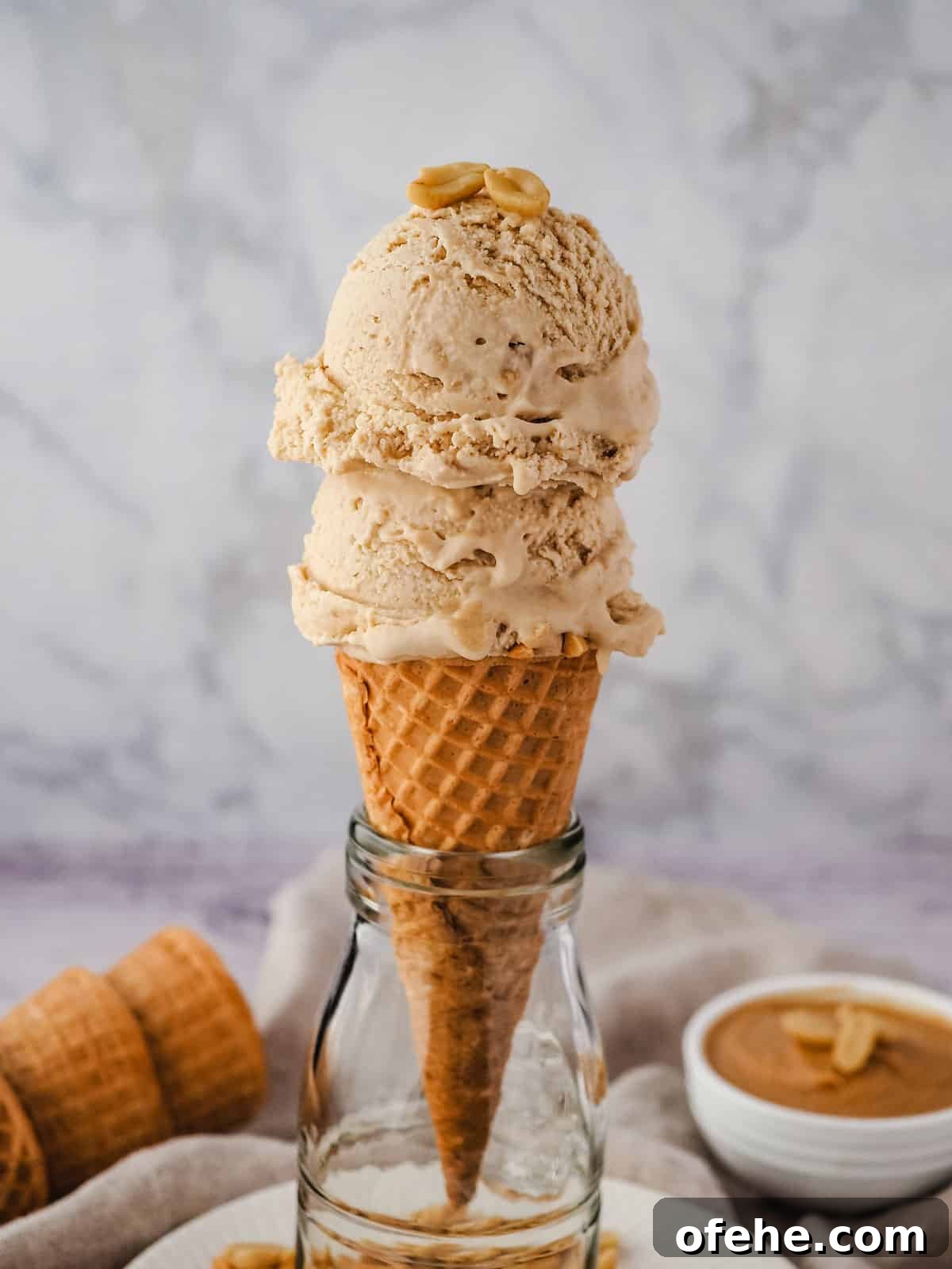 Creamy Peanut Butter Ice Cream Recipe for Homemade Treat 11 Two scoops of ice cream in a cone with roasted peanuts on top.