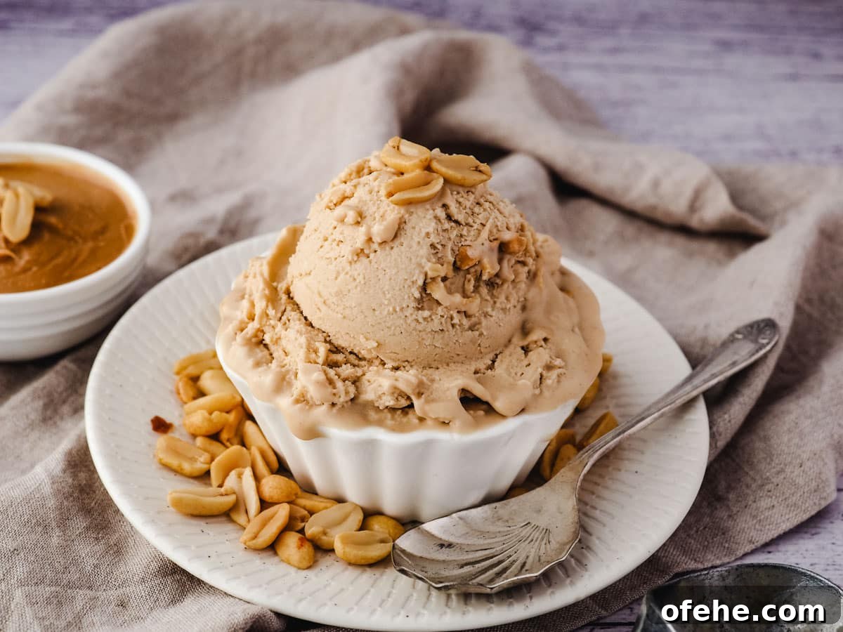 Creamy Peanut Butter Ice Cream Recipe for Homemade Treat 9 Scoop of ice cream in a bowl with roasted peanuts, and a spoon on the side.