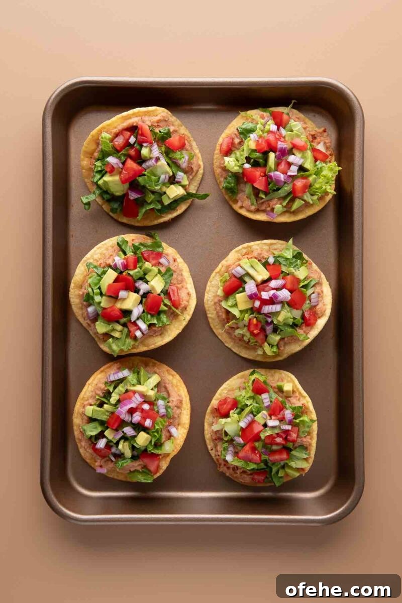 Crispy Mini Tostadas: Party-Ready Bite-Sized Tacos 5 tostadas topped with refried beans, lettuce, tomato, avocado, and red onions