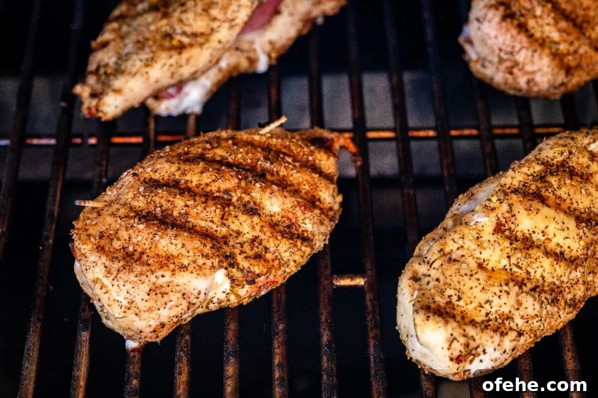 Crispy Grilled Chicken Cordon Bleu Recipe with Ham & Melty Cheese 4 Stuffed chicken breasts on smoker grates with grill marks on top.