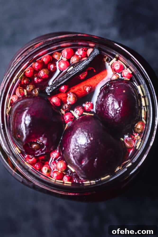 Quick Pickled Fruit: Perfect Brine Ratio for Every Batch 11 overhead shot of pickled cherries in jar. can see 3 cherries, vanilla, cinnamon, pink peppercorns, rosemary and pickling brine in the jar too.