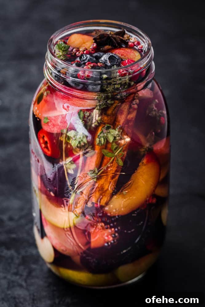 Quick Pickled Fruit: Perfect Brine Ratio for Every Batch 12 Mixed Pickled Fruit! Different fresh fruit in a jar with start anis, pink peppercorns, chili, thyme and pickling brine; side angle shot.