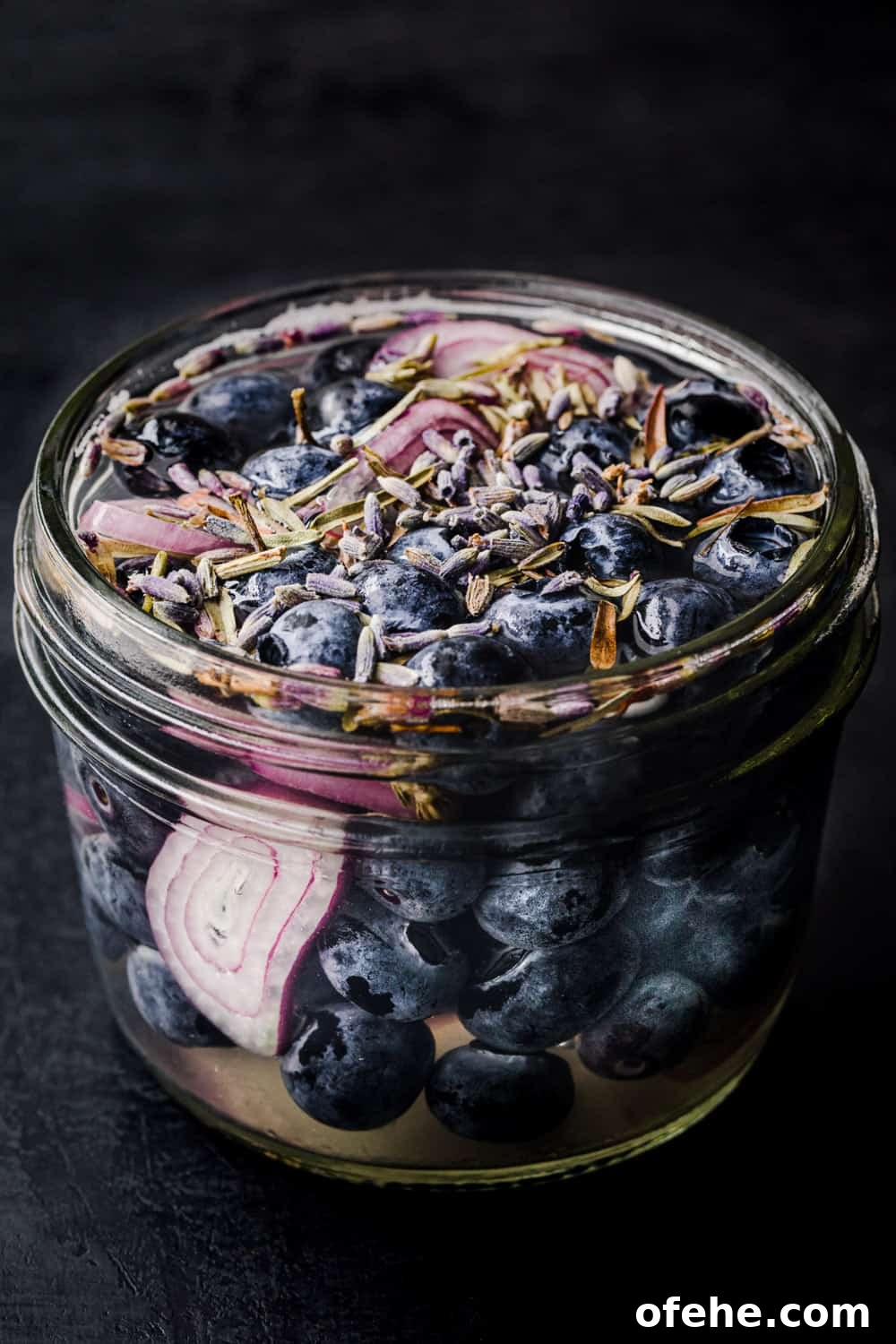 Quick Pickled Fruit: Perfect Brine Ratio for Every Batch 9 Side angle shot of pickled blueberries in a jar with shallots, lavender, thyme and pickling brine.