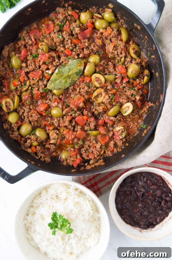 Authentic Brazilian Picadillo (Picadinho) Recipe for Dinner 11 Brazilian picadillo in a black braising pan sits next to a white bowl of rice and a small white bowl holding black beans