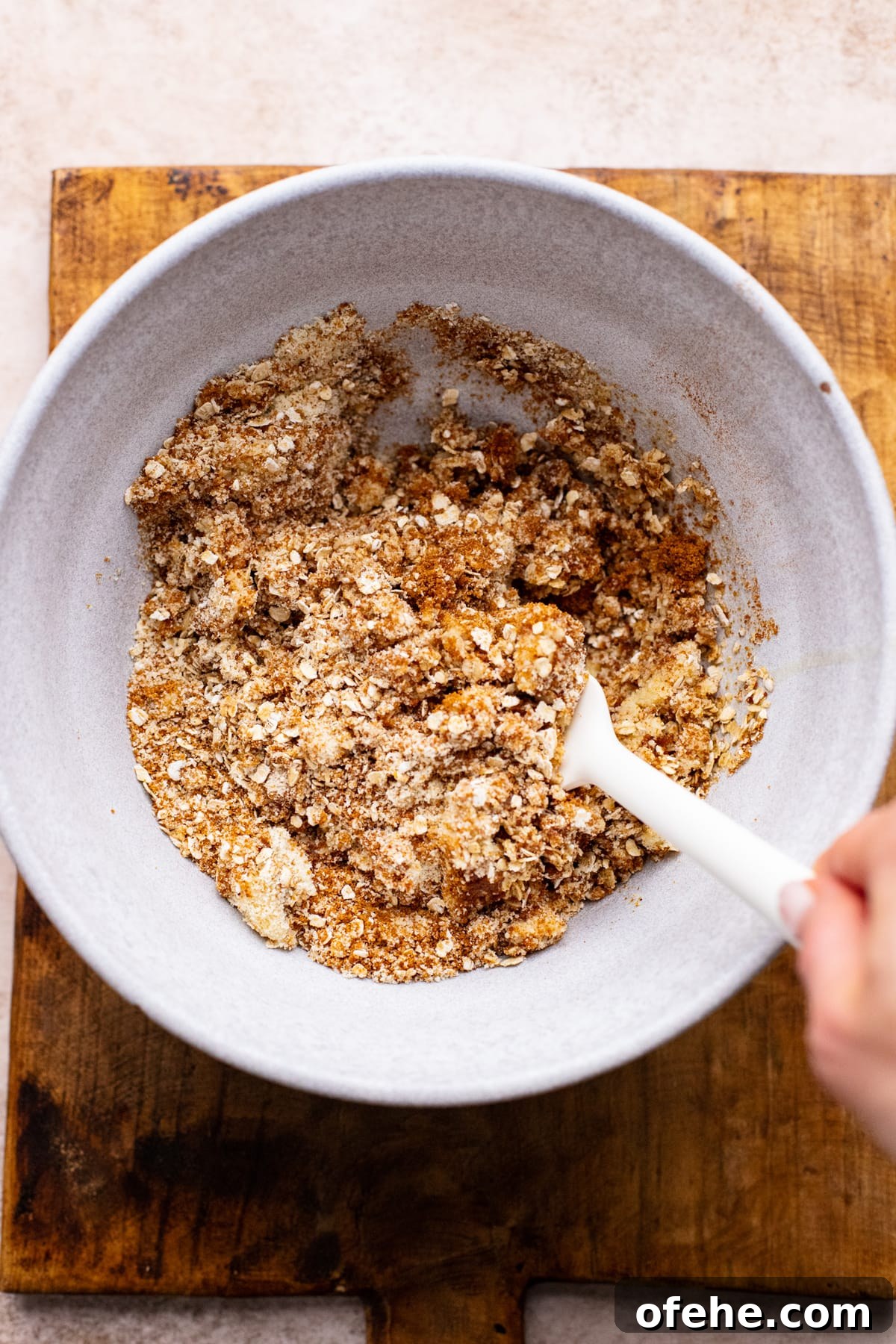 Gluten-Free Strawberry Rhubarb Crisp Recipe for Summer Dessert 5 hand using rubber spatula to mix fruit crisp topping in white bowl.