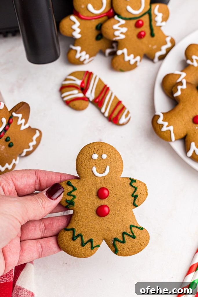 Chewy Air Fryer Gingerbread Cookies Recipe 3 Hand holding golden gingerbread man decorated with frosting.