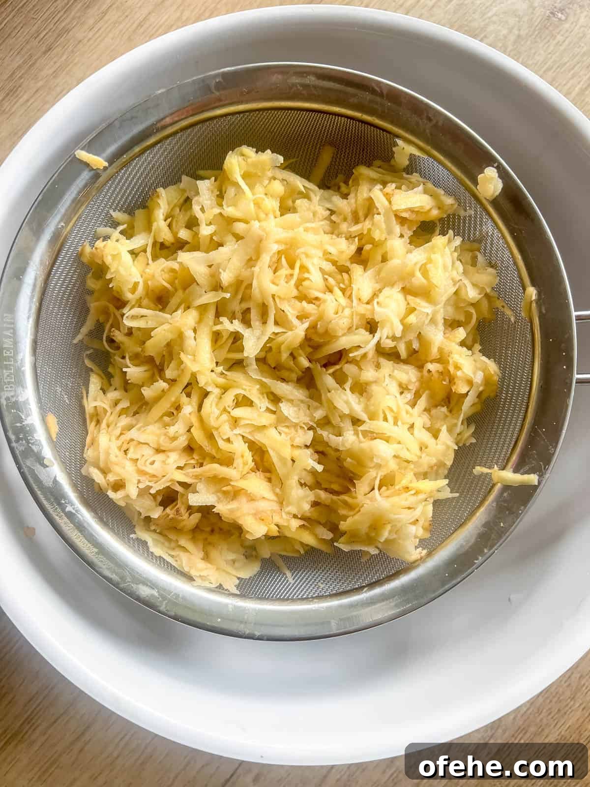 Gluten-Free Potato Pancakes with Optional Whole30 Version 5 Straining shredded potatoes over a bowl.