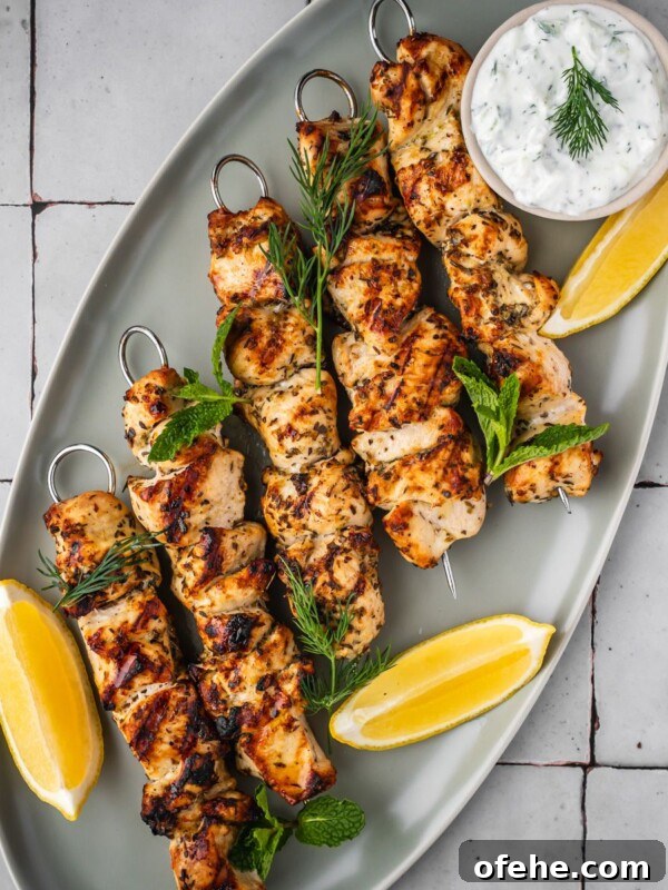 Persian Saffron Joojeh Kabob Recipe — Grilled Chicken Kabab 12 Chicken souvlaki skewers on a platter garnished with dill, mint, sliced lemons and a side of yogurt sauce.