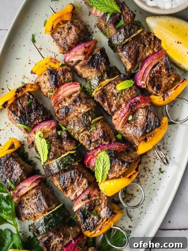 Persian Saffron Joojeh Kabob Recipe — Grilled Chicken Kabab 14 Middle Eastern Beef Shish Kebabs with yellow bell peppers, red onions, and zucchini on skewers, garnished with fresh mint and parsley.