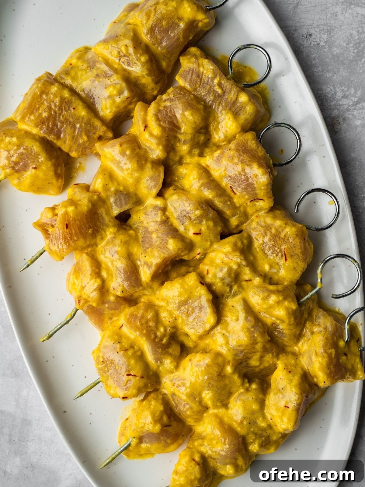 Persian Saffron Joojeh Kabob Recipe — Grilled Chicken Kabab 7 Persian saffron chicken skewers on an oval platter waiting to be grilled.