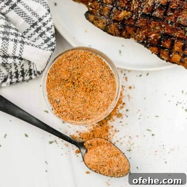 A glass jar and a spoon filled with orange-brown Texas Roadhouse Steak Seasoning sit on a white surface