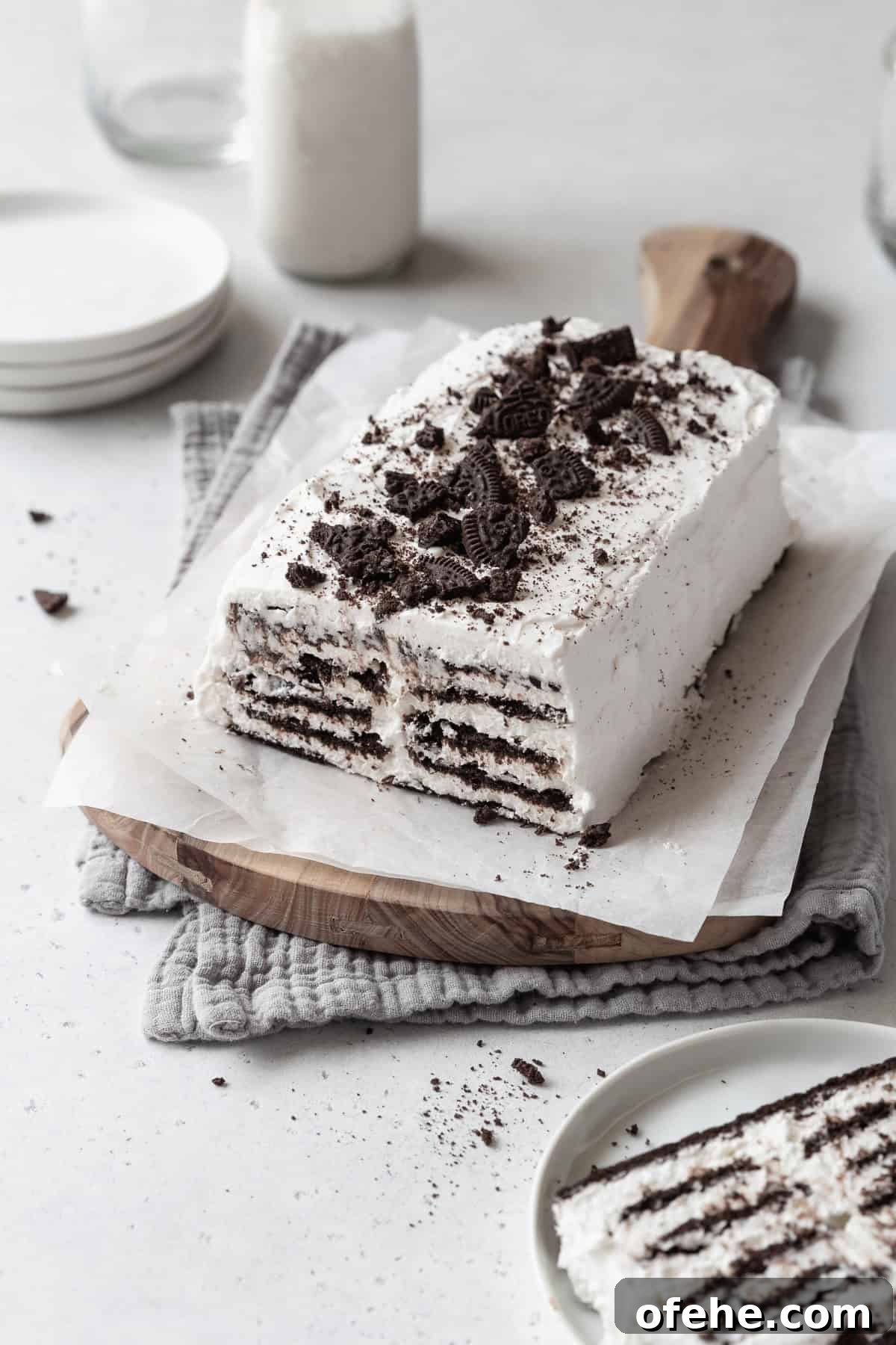 No-Bake Icebox Cake Recipe for Creamy Layered Dessert 3 A loaf of icebox cake with cookie crumbs on top on a parchment paper lined wooden board.