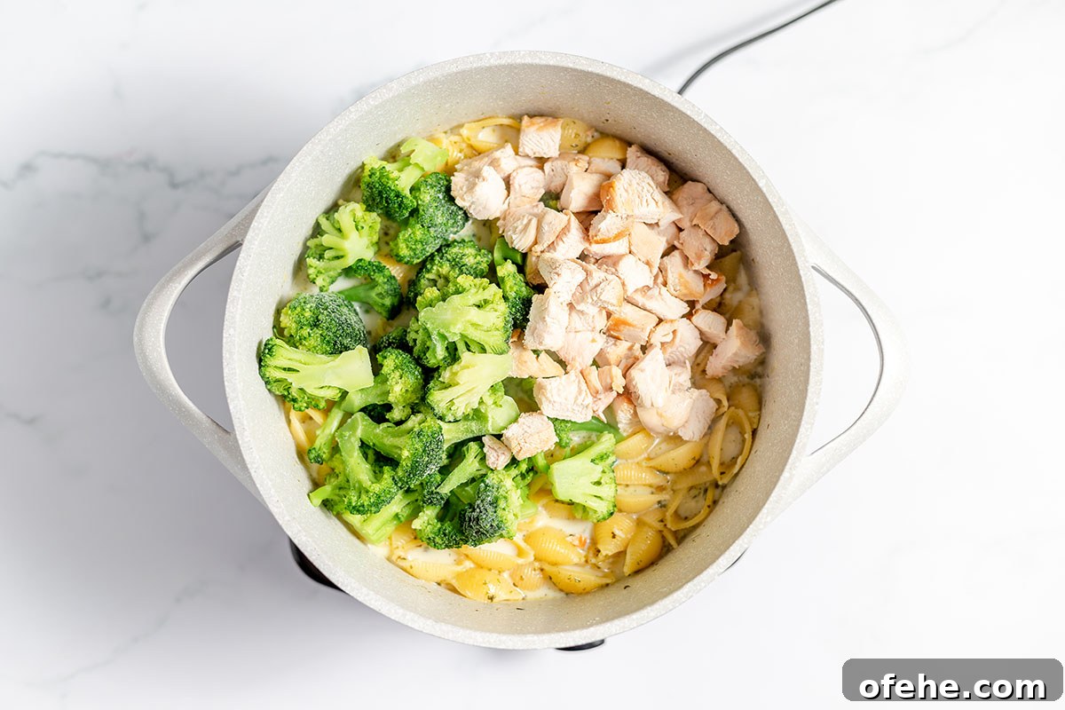 Broccoli and chicken are added to the pasta in the Dutch oven.