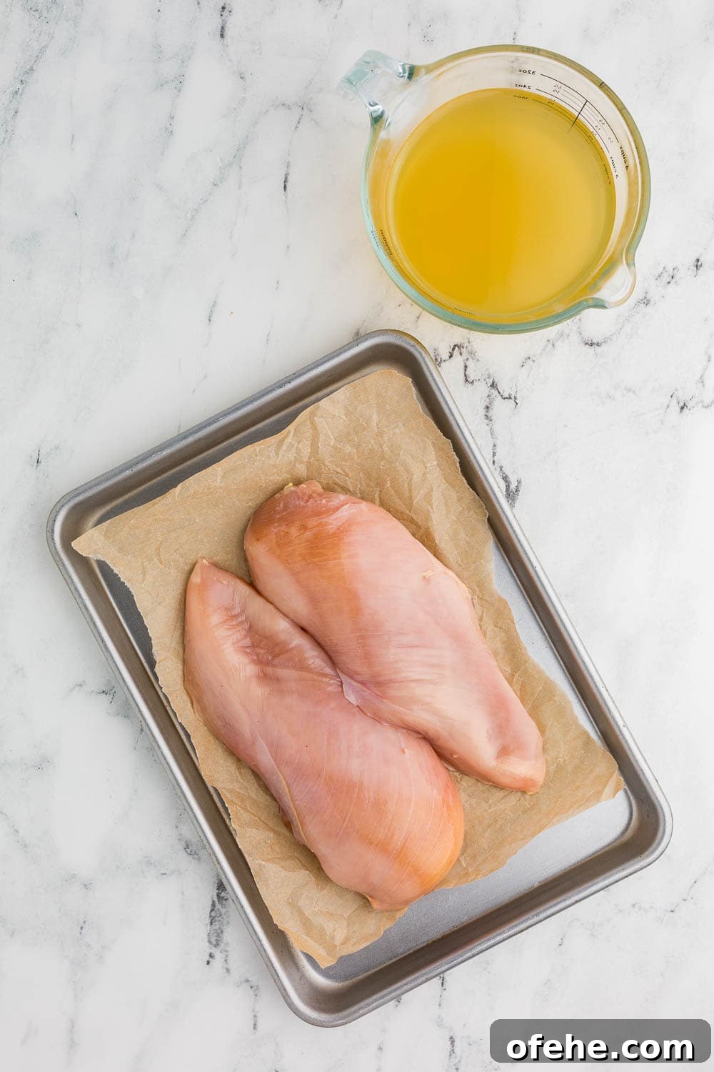 Slow Cooker Shredded Chicken Recipe for Tender, Juicy Meat 3 2 chicken breasts on a baking dish and parchment paper next to measuring cup with chicken broth