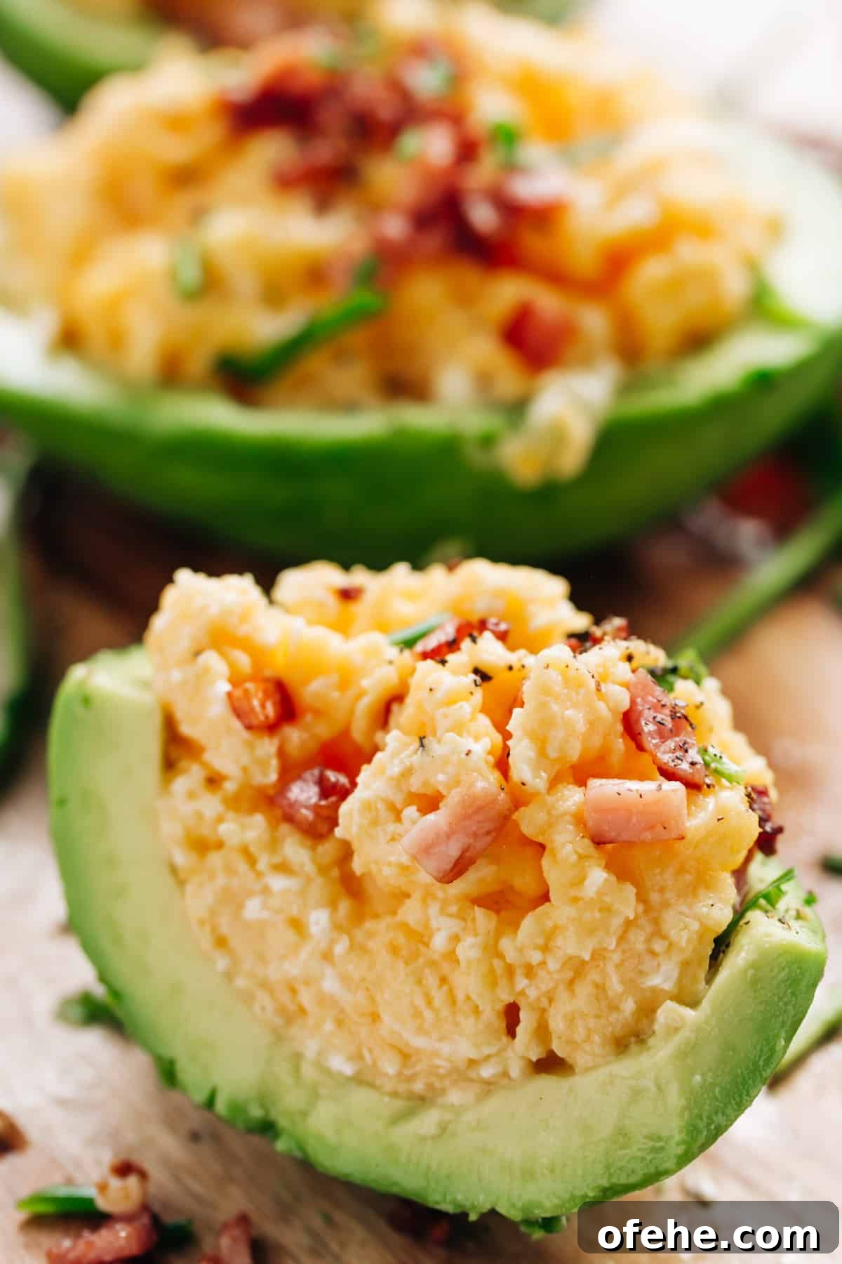 Creamy Avocado Scrambled Eggs Recipe for Quick Breakfast 12 Side view of Scrambled eggs topped with bacon and cracked pepper, stuffed into half avocado, cut in half again to display inside.