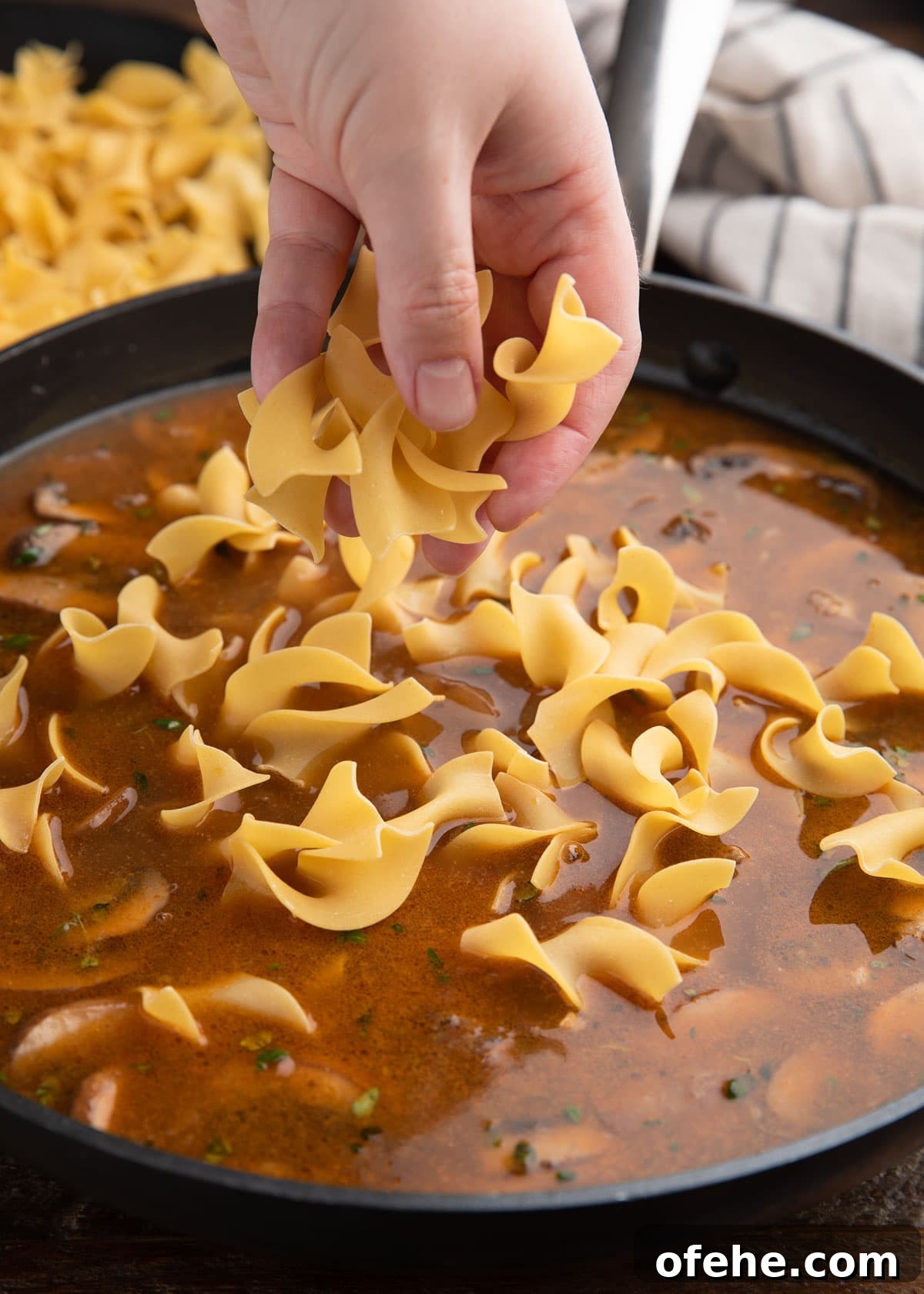 One-Pan Creamy Ground Beef Stroganoff Recipe 6 adding extra wide egg noodles to beef broth in a skillet