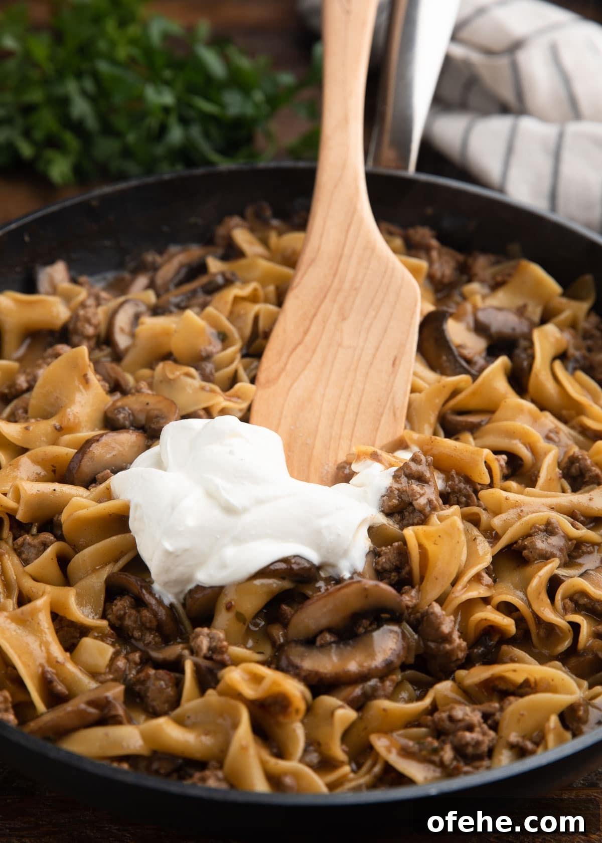One-Pan Creamy Ground Beef Stroganoff Recipe 7 stirring sour cream into ground beef stroganoff with a wooden spoon