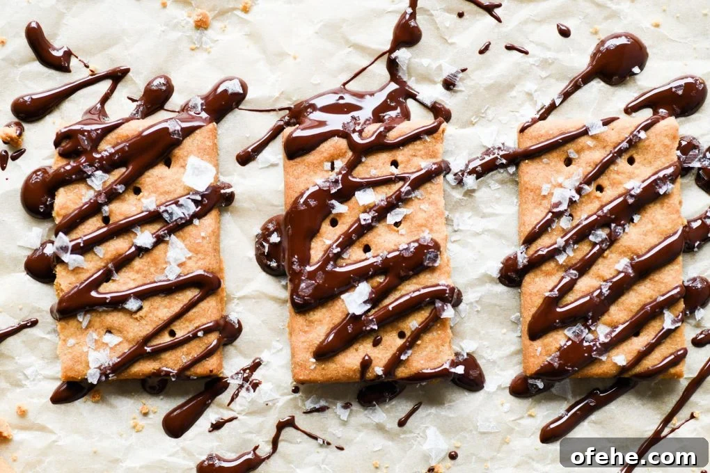 Overhead view of graham crackers drizzled with melted chocolate and topped with flaky sea salt, on light brown parchment paper.