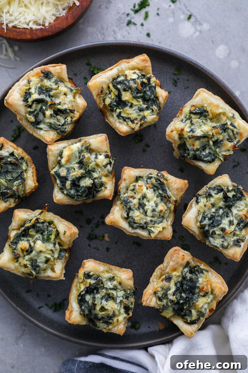 Crispy Baked Spinach and Artichoke Bites You'll Love 6 Golden and flakey baked spinach artichoke bites sitting on a serving tray sprinkled with fresh parsley