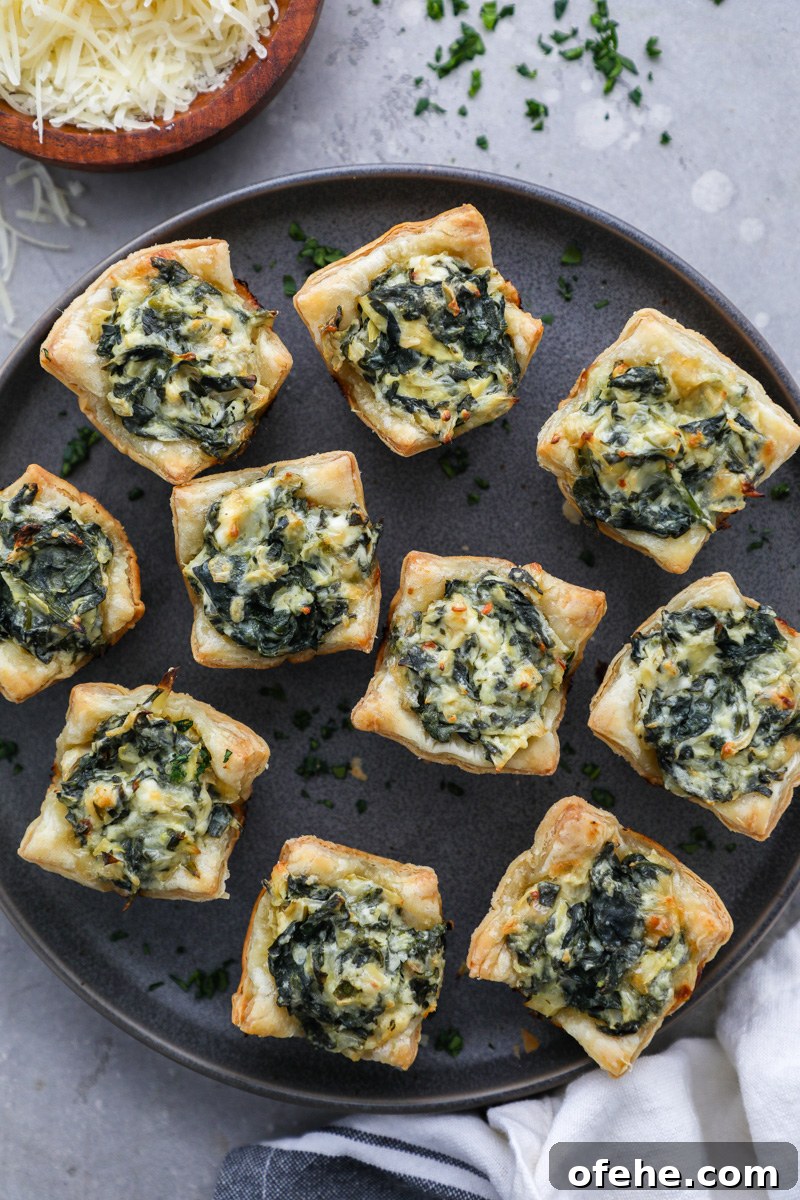 Crispy Baked Spinach and Artichoke Bites You'll Love 7 A small serving plate filled with healthier spinach artichoke bites sitting next to a bowl of shredded parmesan