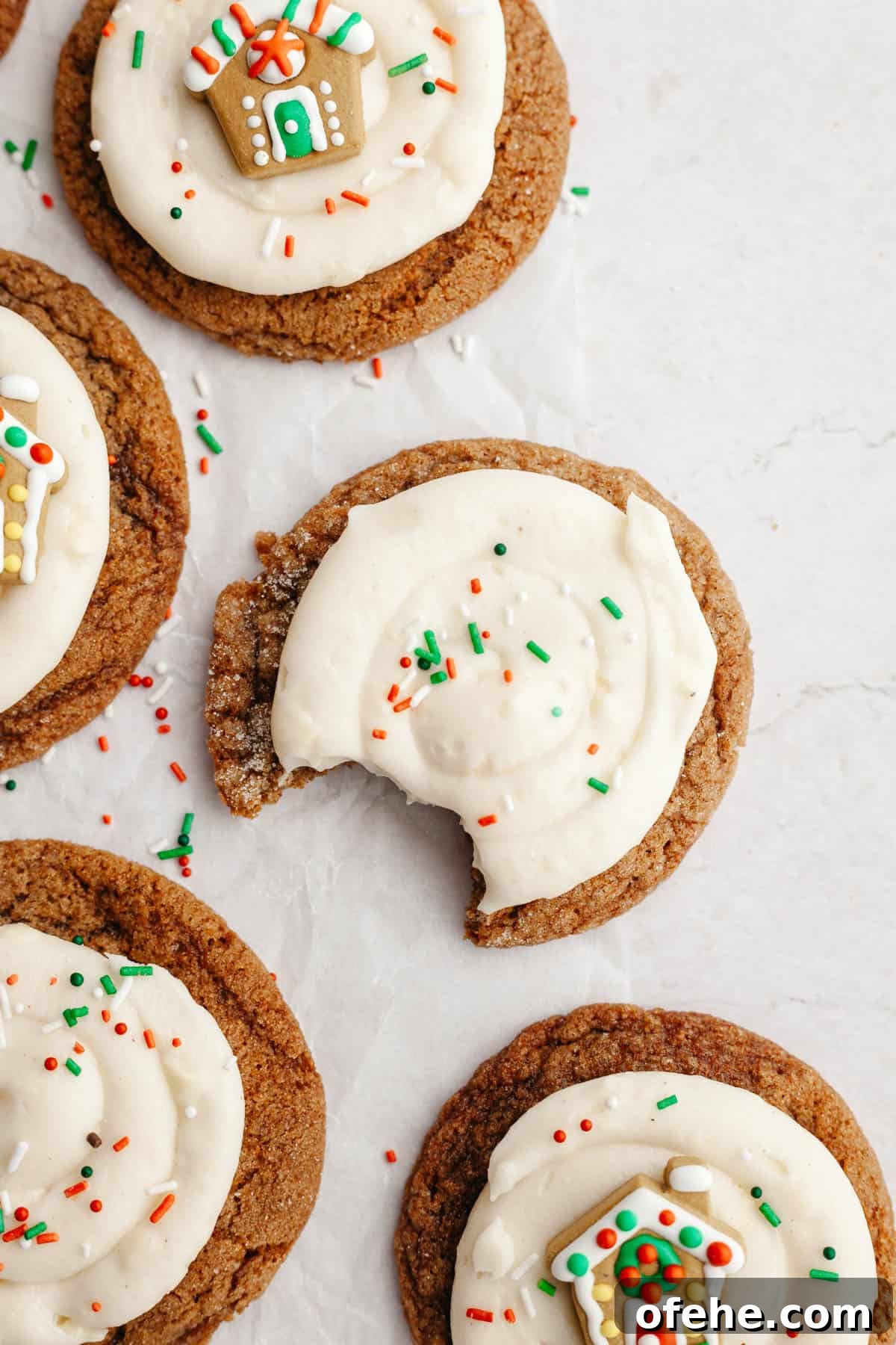 Soft Frosted Gingerbread Cookies with Cream Cheese Frosting Recipe 11 A close up of gingerbread cookies frosted with cream cheese frosting and a small gingerbread house decoration and sprinkles.