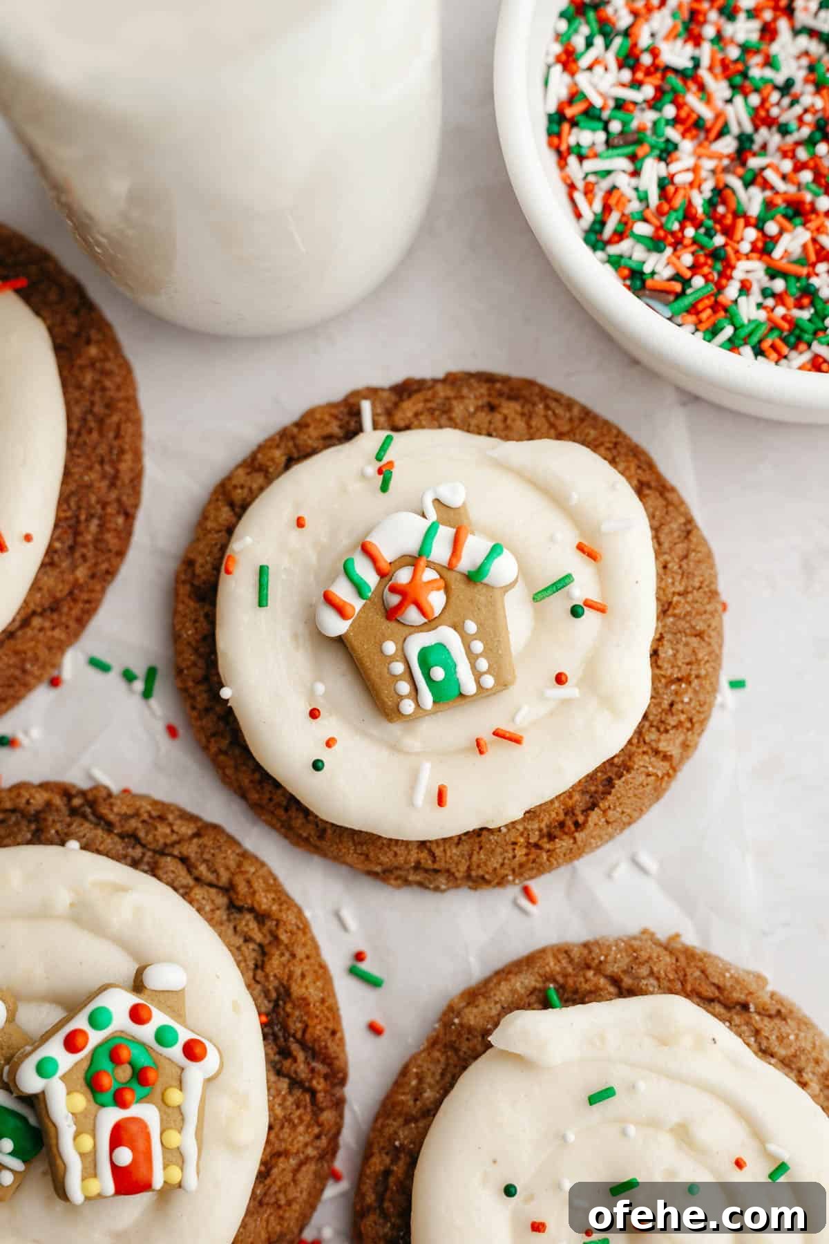Soft Frosted Gingerbread Cookies with Cream Cheese Frosting Recipe 13 A close up of gingerbread cookies frosted with cream cheese frosting and a small gingerbread house decoration.