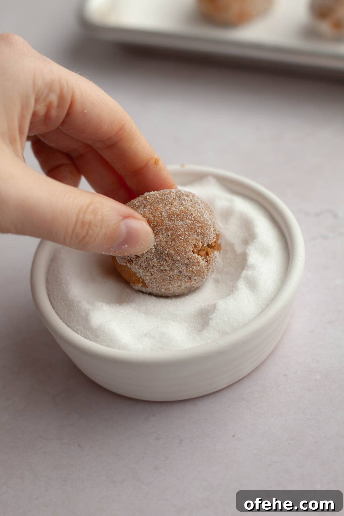 Soft Frosted Gingerbread Cookies with Cream Cheese Frosting Recipe 8 A hand rolling a cookie dough ball in sugar.