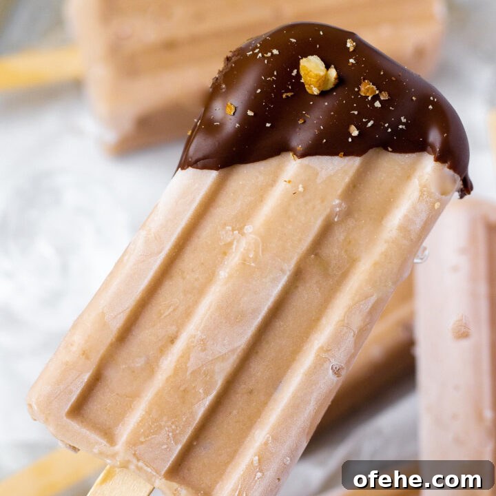 a light brown banana popsicle with just the top dipped in chocolate, sprinkled with chopped walnuts