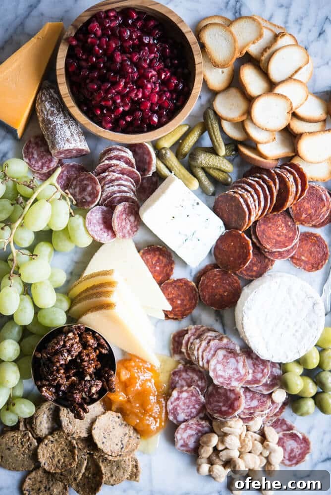 Build a Stunning Charcuterie Board: Expert Tips for Entertaining 2 Charcuterie board with meats, cheeses, honey, nuts, a wooden bowl of pomegranates, olives, grapes, pickles, crackers, on a marble board