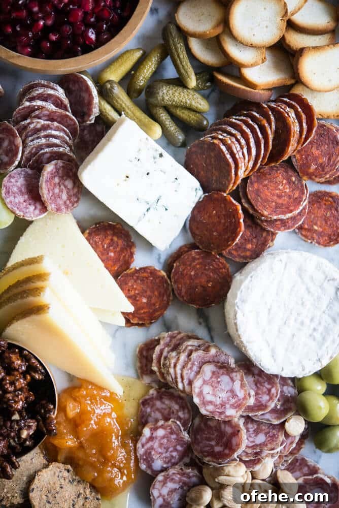 Build a Stunning Charcuterie Board: Expert Tips for Entertaining 3 Charcuterie board with meats, cheeses, honey, nuts, a wooden bowl of pomegranates, olives, grapes, pickles, crackers, on a marble board