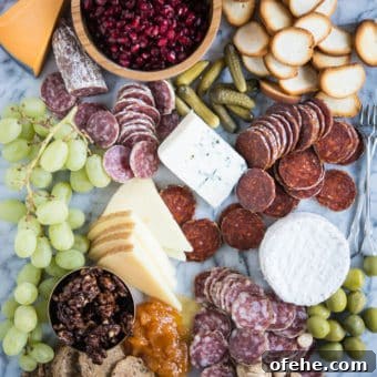 Build a Stunning Charcuterie Board: Expert Tips for Entertaining 5 Charcuterie board with meats, cheeses, honey, nuts, a wooden bowl of pomegranates, olives, grapes, pickles, crackers, on a marble board