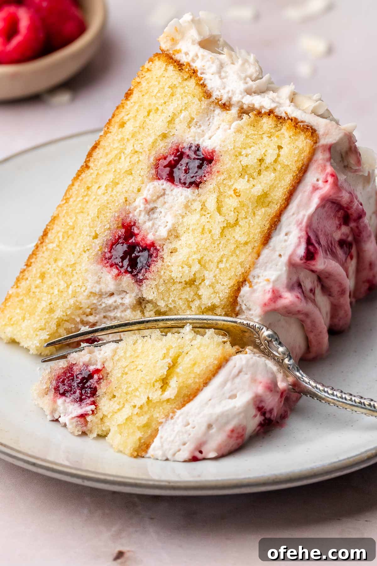 Raspberry Coconut Cake Recipe with Creamy Coconut Frosting 2 A slice of coconut raspberry cake on a plate with a fork cutting into it.
