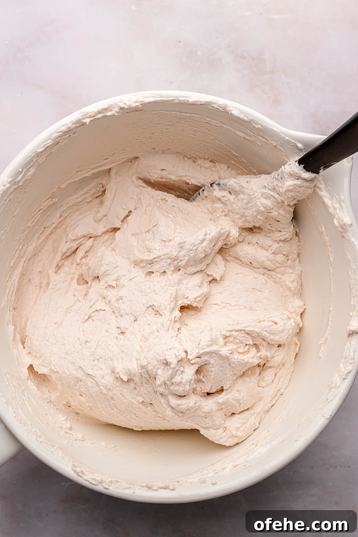 Raspberry Coconut Cake Recipe with Creamy Coconut Frosting 11 A spatula folds whipped cream cheese frosting together.