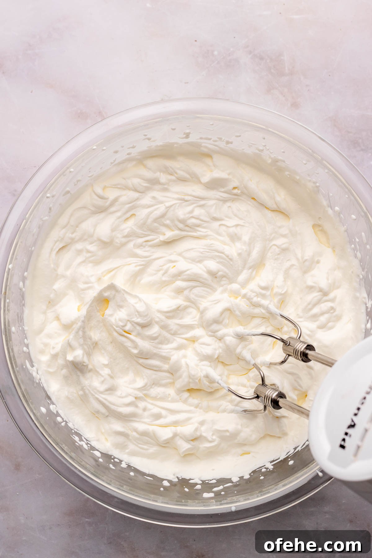 Raspberry Coconut Cake Recipe with Creamy Coconut Frosting 9 A hand mixer beats whipped cream in a bowl.