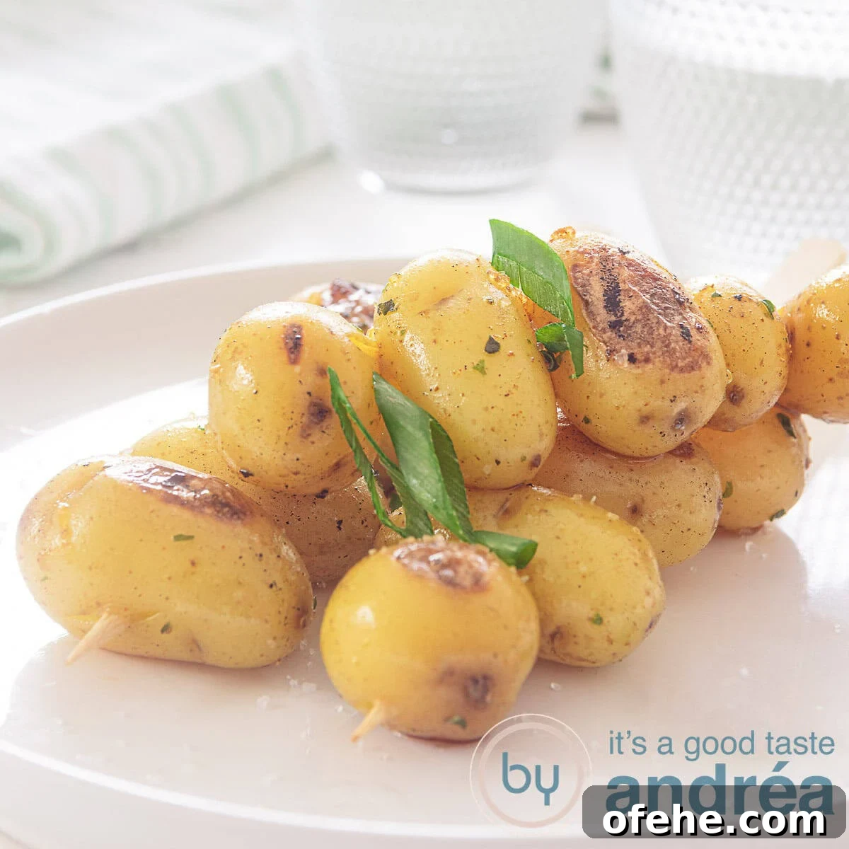 Grilled BBQ Baby Potato Skewers – Savory Summer Side Dish 4 A square photo with a white plate with three baby potatoes skewers with spring onions. A white background