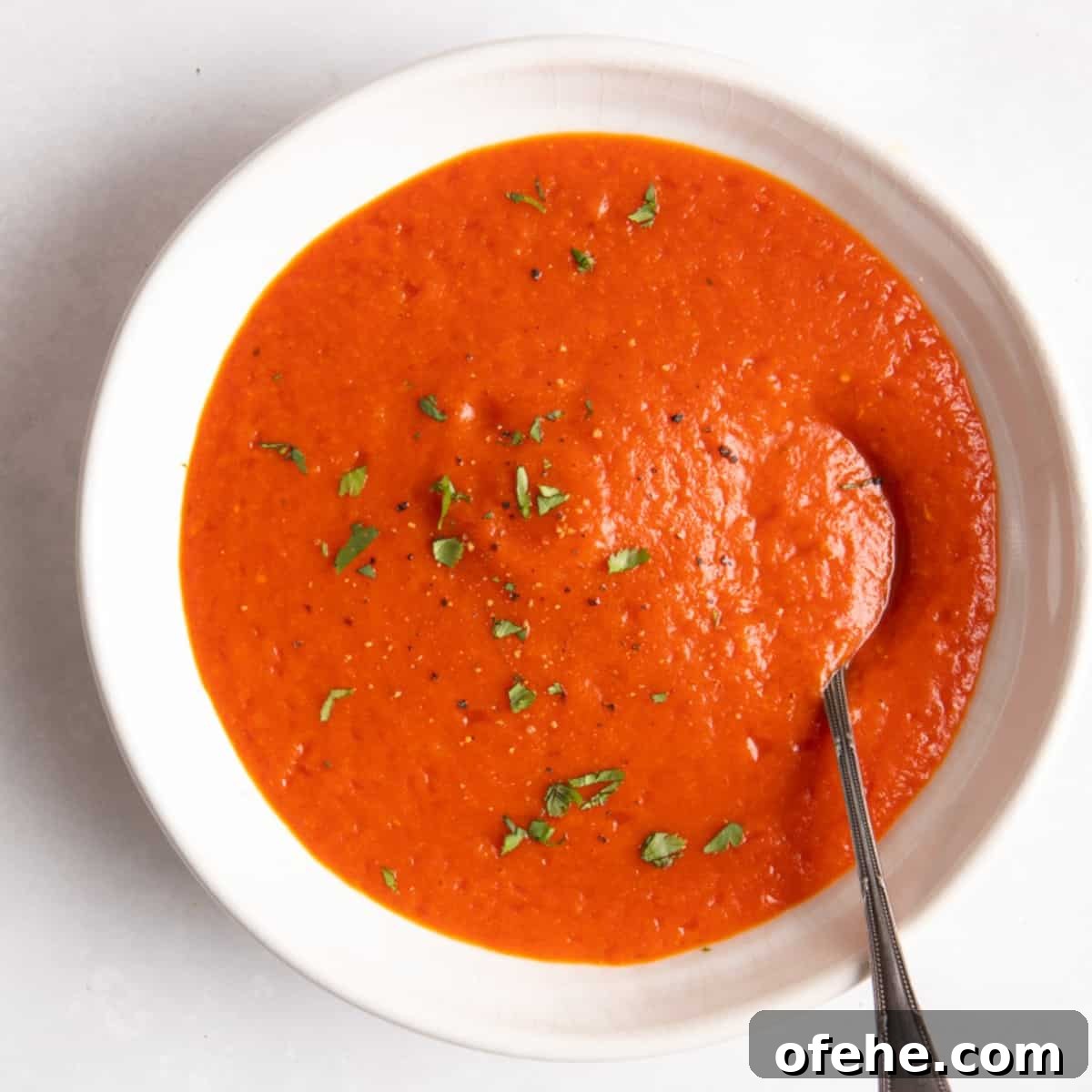 Roasted Red Pepper & Tomato Soup Recipe for Cozy Weeknights 2 Red Pepper & Tomato Soup served in a white bowl with a spoon on a white background.