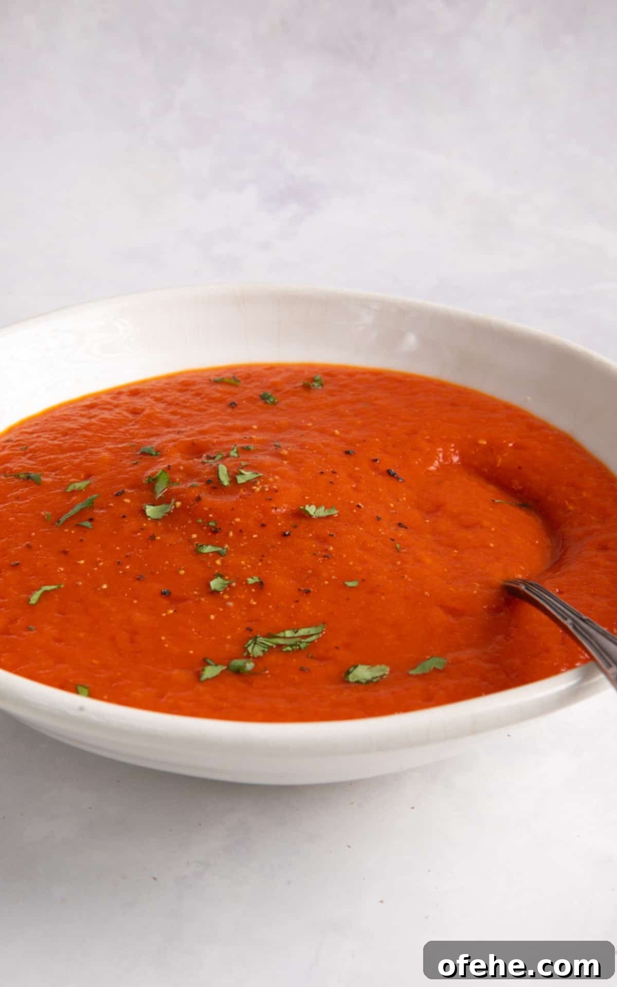 Roasted Red Pepper & Tomato Soup Recipe for Cozy Weeknights 7 roasted red pepper and tomato soup served in a white bowl with a spoon.