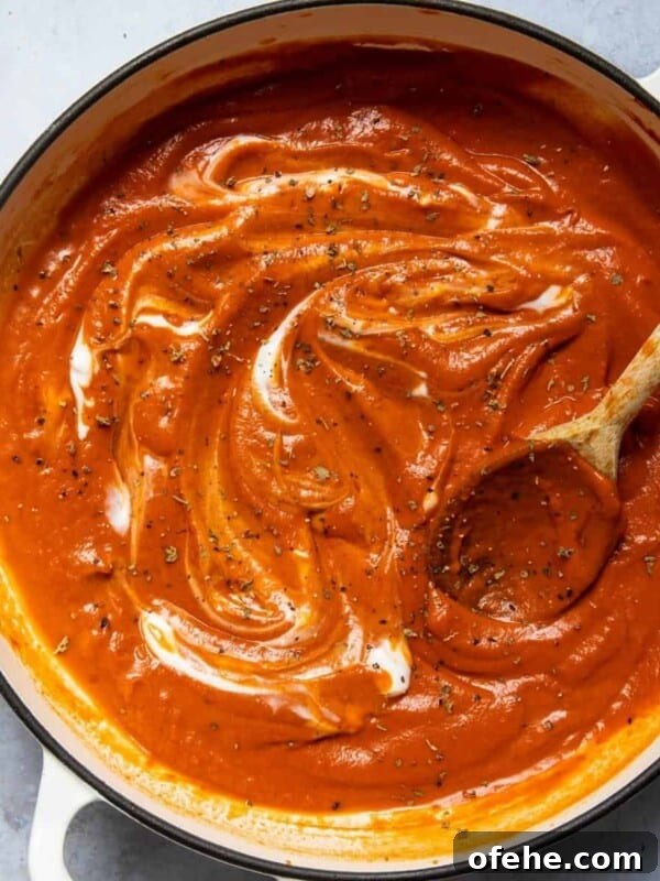 Roasted Red Pepper & Tomato Soup Recipe for Cozy Weeknights 8 Tomato soup in a large pot with a wooden spoon. Pot is displayed on a white marble background.