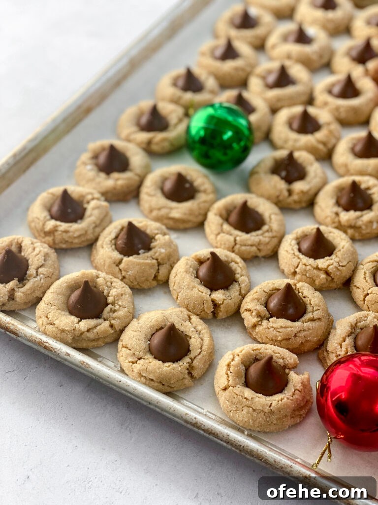 Classic Peanut Butter Blossom Cookies Recipe — Chewy & Chocolate-Topped 4 cookies lined up across a cookie sheet with a few ornaments instead of cookies