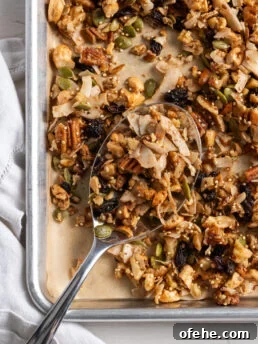 silver spoon on the bottom left corner of a parchment lined baking sheet scooping up some healthy grain free granola.