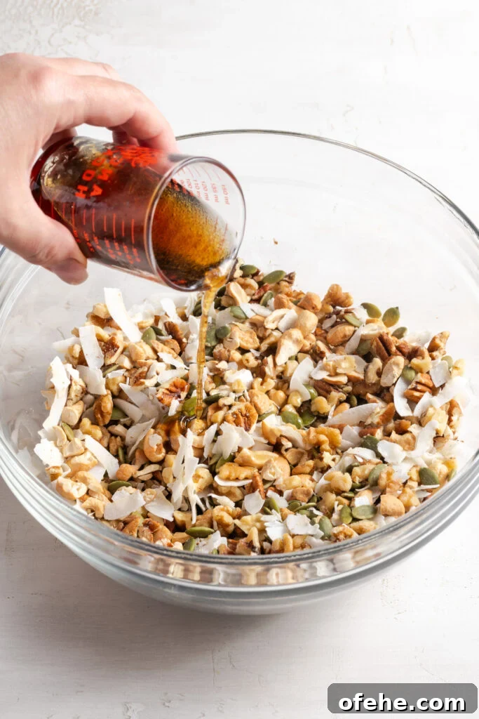 Grain-Free Homemade Granola Recipe with Crunchy Seeds 8 action shot of hand pouring the liquid ingredients over the dry grain free granola mixture.