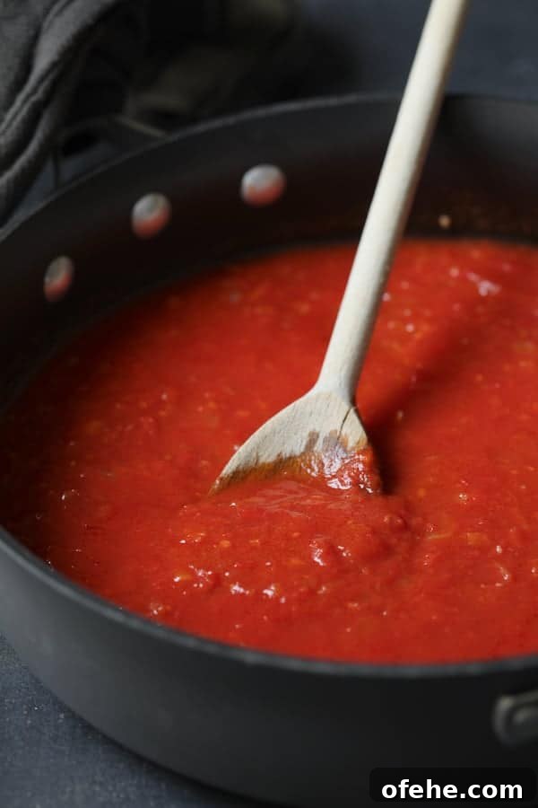 Middle Eastern Meatballs Simmered in Spiced Tomato Sauce 4 Photo of tomato sauce in skillet being stirred with wooden spoon.