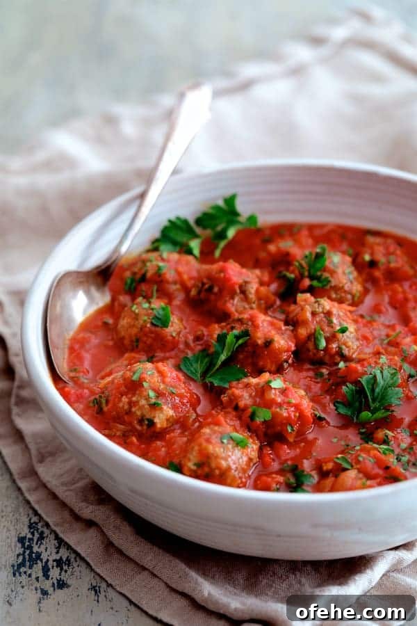 Middle Eastern Meatballs Simmered in Spiced Tomato Sauce 5 Photo of Middle Eastern Meatballs in Tomato Sauce in white serving bowl with serving spoon garnished with parsley.
