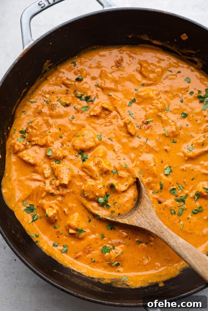 Top view of chicken paprikash in a pan with a wooden spoon.