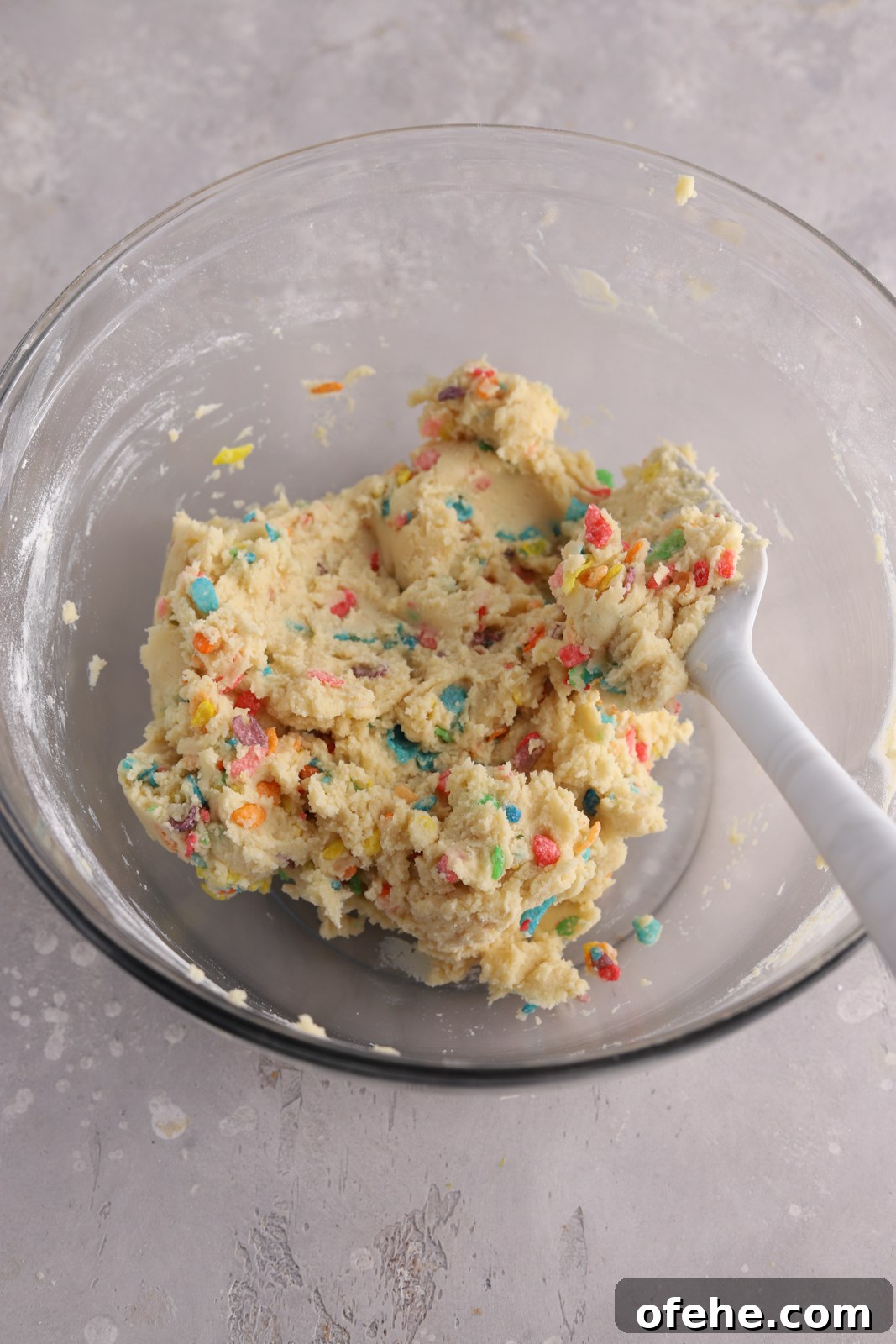 Fruity Pebbles Cookies Recipe: Colorful, Crispy Treats 5 Cookie dough with Fruity Pebbles cereal in it in a bowl with a spatula.